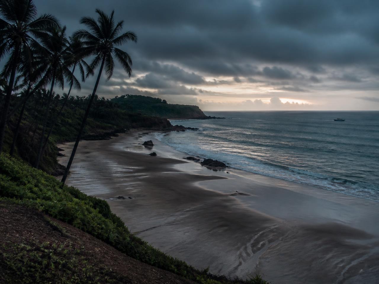 Monsoon dusk over a Goan beach, palms silhouetted against heavy cloud and a grey sea