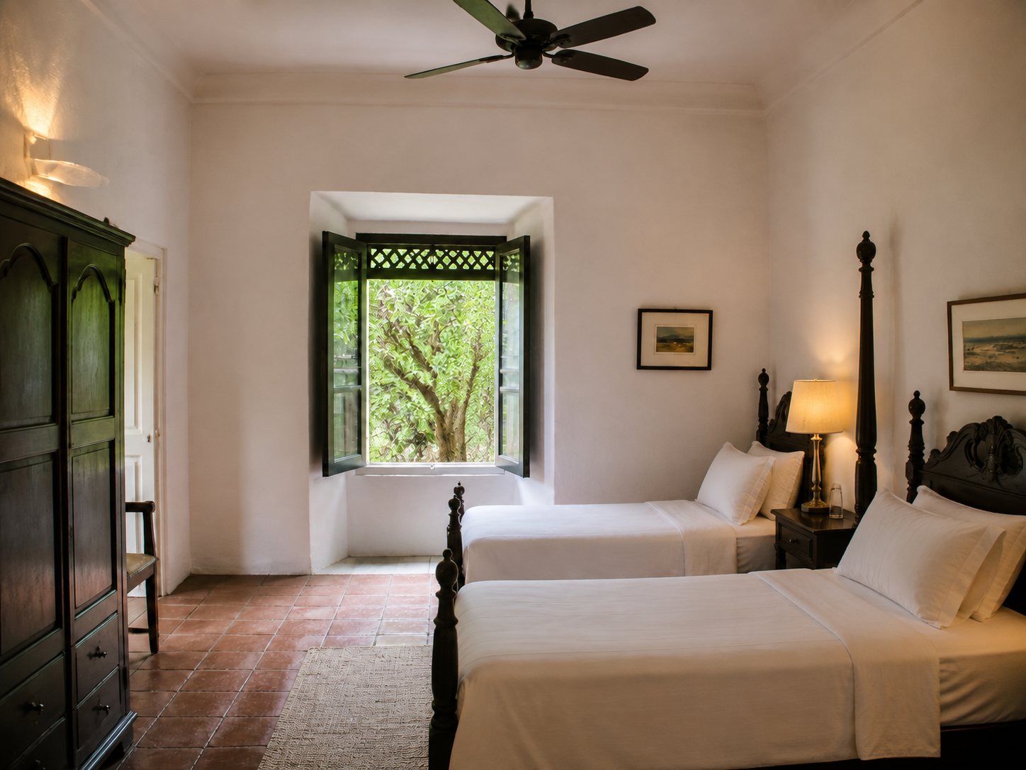 A whitewashed villa bedroom with a dark wood four-poster bed and open shuttered window onto green foliage